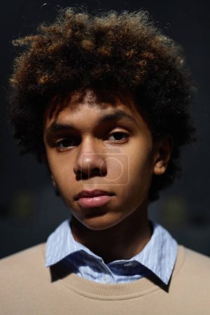 Téléchargez les photos : Portrait vertical d'un adolescent afro-américain regardant une caméra sur fond noir - en image libre de droit