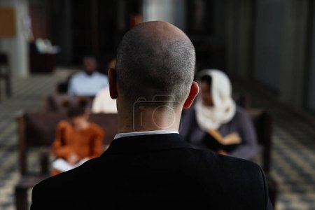 Foto de Vista trasera de protestante en traje negro leyendo la Biblia para los creyentes mientras están sentados en el banco en la iglesia bautista - Imagen libre de derechos
