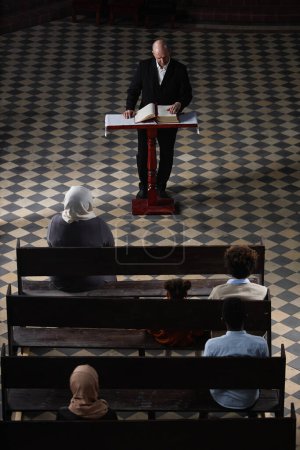 Foto de Vista de ángulo alto del pastor maduro en traje negro de pie y la oración de lectura para los creyentes en la iglesia - Imagen libre de derechos