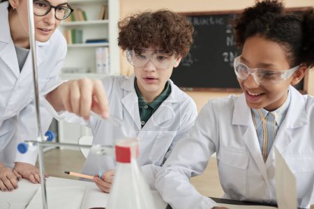 Téléchargez les photos : Portrait d'un garçon faisant une expérience scientifique en classe avec un groupe d'enfants portant des blouses de laboratoire - en image libre de droit