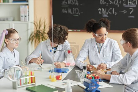 Photo for Diverse group of schoolchildren wearing lab coats during science experiment class in school - Royalty Free Image