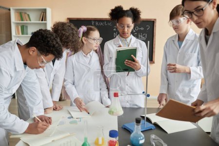 Téléchargez les photos : Groupe diversifié de jeunes adolescents portant des blouses de laboratoire profitant d'expériences scientifiques à l'école ensemble - en image libre de droit