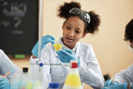 Téléchargez les photos : Portrait d'écolière adolescente noire appréciant les expériences scientifiques à l'école et travaillant avec la réaction chimique - en image libre de droit