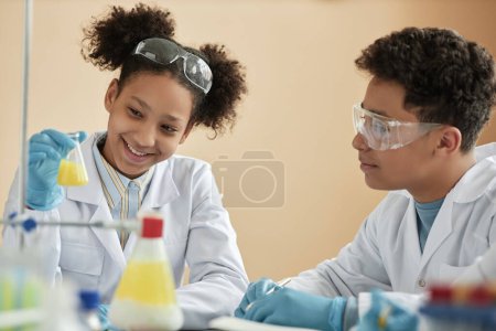 Téléchargez les photos : Portrait de sourire fille noire profiter des expériences scientifiques à l'école et regarder la réaction chimique - en image libre de droit