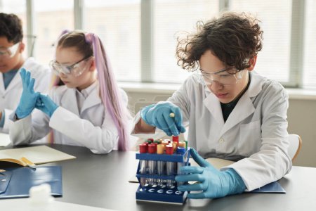 Photo for Portrait of curly haired teen schoolboy looking at beakers in science class and enjoying experiments - Royalty Free Image