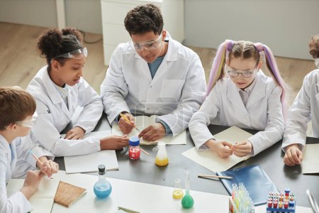 Téléchargez les photos : Vue d'ensemble d'un groupe diversifié d'enfants faisant des expériences en classe de sciences à l'école et portant des blouses de laboratoire - en image libre de droit