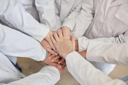 Photo for Top view closeup of group of children stacking hands in science class with white lab coats - Royalty Free Image