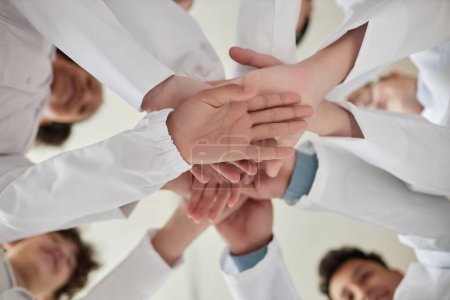 Photo for Up view closeup of children stacking hands in science class and wearing white lab coats - Royalty Free Image
