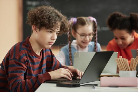 Photo for Side view portrait of teenage schoolboy using laptop computer in school classroom, copy space - Royalty Free Image