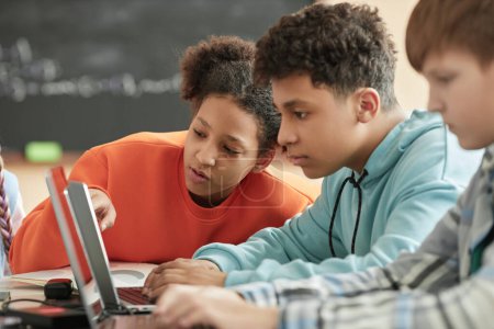 Children using laptop in school classroom focus on black girl looking at computer screen