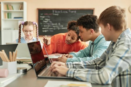 Photo for Diverse group of children using laptops in school classroom with black girl peeking at computer screen - Royalty Free Image