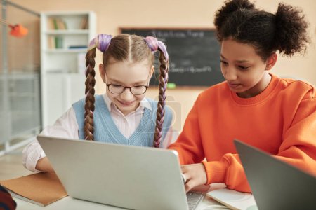Téléchargez les photos : Portrait de deux écolières adolescentes utilisant un ordinateur portable ensemble dans la salle de classe en regardant l'écran d'ordinateur - en image libre de droit