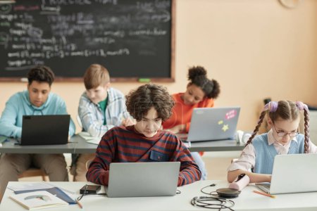 Téléchargez les photos : Groupe d'écoliers utilisant des ordinateurs portables en classe pendant la leçon de programmation - en image libre de droit