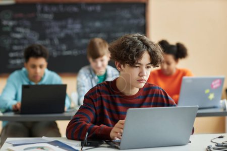 Téléchargez les photos : Portrait d'un écolier utilisant un ordinateur portable en classe pendant une leçon de programmation - en image libre de droit