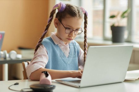 Téléchargez les photos : Portrait d'une écolière utilisant un ordinateur portable en classe pendant une leçon de programmation pour enfants - en image libre de droit