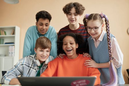 Téléchargez les photos : Groupe d'écoliers joyeux utilisant un ordinateur portable en classe pendant la leçon de programmation - en image libre de droit