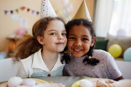 Portrait de deux petites filles heureuses regardant la caméra tout en profitant de fête d'anniversaire ensemble.