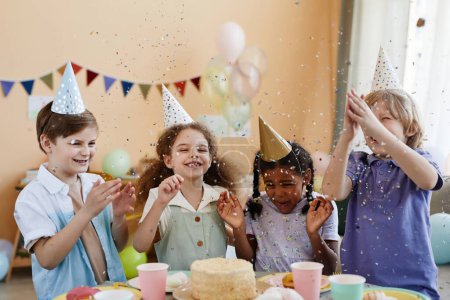 Foto de Diverso grupo de niños emocionados lanzando confeti mientras disfruta de la fiesta de cumpleaños para niños y se divierte - Imagen libre de derechos