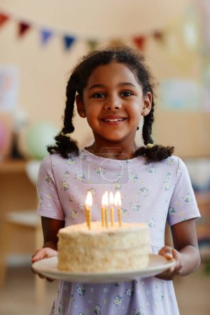 Foto de Cintura vertical hacia arriba retrato de niña negra sosteniendo pastel de cumpleaños con velas y sonriendo a la cámara - Imagen libre de derechos