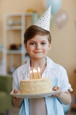 Foto de Cintura vertical hacia arriba retrato de niño feliz sosteniendo pastel de cumpleaños con velas y mirando a la cámara - Imagen libre de derechos