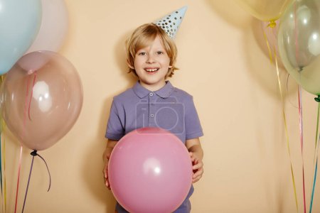 Photo for Minimal waist up portrait of happy boy holding balloon at party and smiling at camera against pastel background - Royalty Free Image