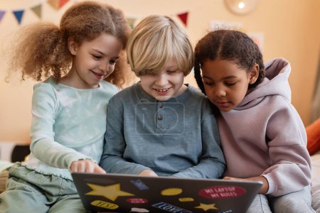 Groupe de trois petits enfants utilisant un ordinateur portable ensemble à la maison et souriant