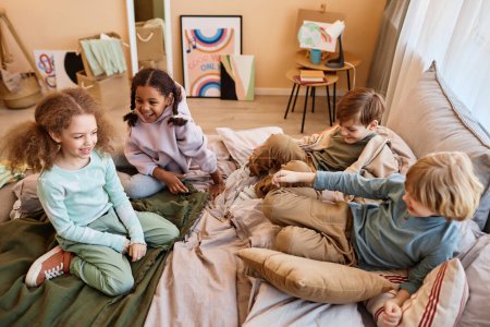 Photo for High angle view at group of happy little children sitting on bed together and chatting - Royalty Free Image