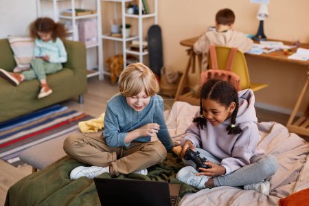 Photo for Portrait of two kids playing videogame on bed with laptop, copy space - Royalty Free Image