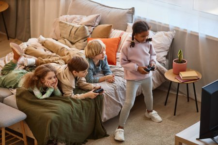 Photo for High angle view at group of children playing videogames together and lying on bed, copy space - Royalty Free Image