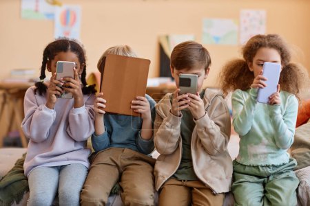 Photo for Group of young children holding smartphones and hiding faces, gen Alpha - Royalty Free Image