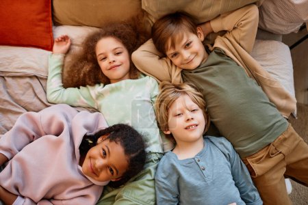 Photo for Top view at diverse group of children lying on bed together and looking at camera - Royalty Free Image