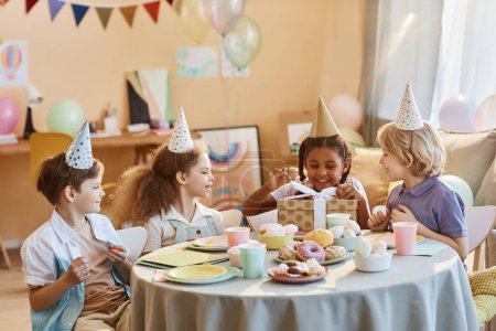 Groupe diversifié d'enfants heureux à la fête d'anniversaire avec des cadeaux d'ouverture de petite fille