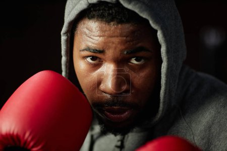 Téléchargez les photos : Gros plan du jeune boxeur afro-américain se concentrant sur le prochain coup de pied tout en se tenant devant le sac de boxe et va le frapper - en image libre de droit