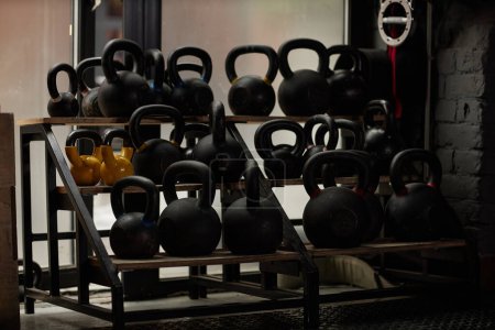 Photo for Large display with group of heavy kettlebells of black and yellow color standing on shelves in the corner of modern sports club or gym - Royalty Free Image