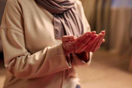 Enfoque en las palmas abiertas de la joven musulmana en jersey beige de pie sobre sus rodillas delante de la cámara durante la gratitud y la oración de adoración
