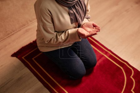 Oben Aufnahme einer jungen Frau in Freizeitkleidung, die auf Knien auf einem kleinen roten Teppich sitzt und beim Gebet die Handflächen offen vor sich hält