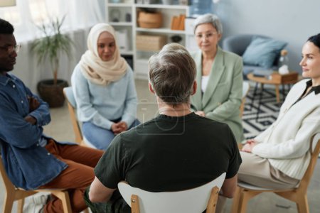 Focus on rear view of mature male patient of counselor sitting in front of other people and psychologist listening to his story during session