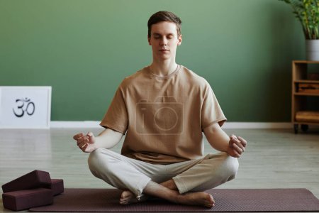 Foto de Retrato de vista frontal de un joven meditando en el interior sentado en posición de loto con los ojos cerrados, espacio para copiar - Imagen libre de derechos