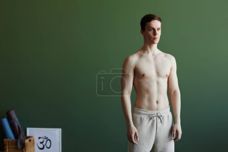 Téléchargez les photos : Portrait taille haute minimaliste de l'homme torse nu yogi homme debout contre le vert et détournant les yeux, copier l'espace - en image libre de droit