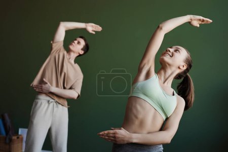 Foto de Retrato de cintura hacia arriba de una joven sonriente haciendo estiramientos en clase de yoga, espacio para copiar - Imagen libre de derechos