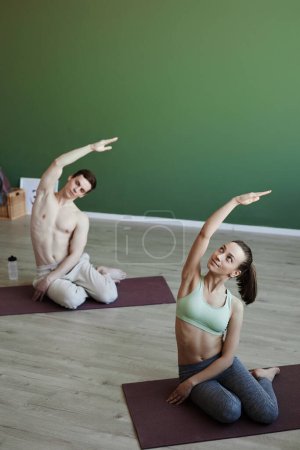 Foto de Retrato vertical de dos jóvenes haciendo estiramientos en interiores en clase de yoga, espacio de copia arriba - Imagen libre de derechos