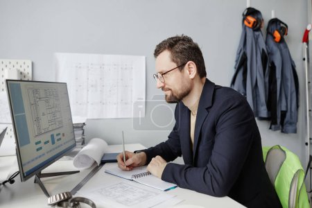 Téléchargez les photos : Portrait latéral d'un ingénieur barbu utilisant un ordinateur sur le lieu de travail au bureau et concevant des plans directeurs - en image libre de droit