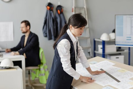 Téléchargez les photos : Vue de côté portrait de la femme asiatique en tant qu'ingénieure dessinant des plans et des plans au poste de travail dans le bureau, espace de copie - en image libre de droit