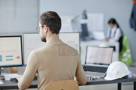 Foto de Vista posterior del hombre adulto barbudo que trabaja como ingeniero en el lugar de trabajo con sombrero en la mesa, espacio de copia - Imagen libre de derechos