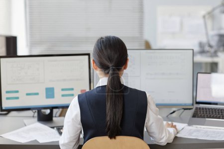 Téléchargez les photos : Vue arrière de la femme qui travaille comme ingénieure à l'aide d'un ordinateur avec des plans à l'écran, espace de copie - en image libre de droit