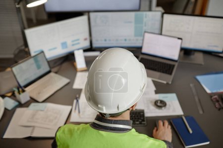 Téléchargez les photos : Vue de dessus de l'ingénieur portant un casque de sécurité sur le lieu de travail au bureau et utilisant un ordinateur, espace de copie - en image libre de droit