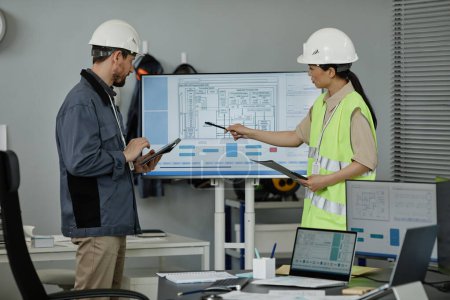 Photo for Side view portrait of two engineers reviewing blueprints indoors and pointing at computer screen, copy space - Royalty Free Image