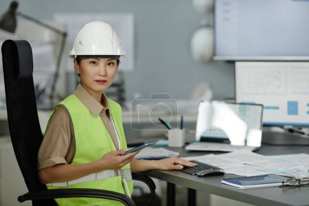 Téléchargez les photos : Portrait de femme asiatique portant un casque de sécurité sur le lieu de travail au bureau et regardant la caméra avec une expression sérieuse du visage, espace de copie - en image libre de droit