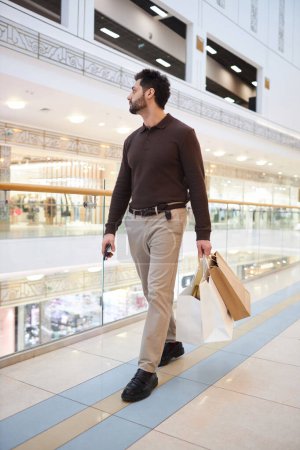 Photo for Vertical full length portrait of man walking in shopping mall and holding bags - Royalty Free Image