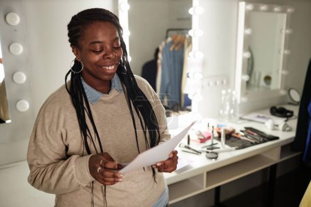 Foto de Retrato de la cintura hacia arriba de una mujer afroamericana sonriente leyendo texto mientras ensayaba para el espacio de copia entre bastidores - Imagen libre de derechos